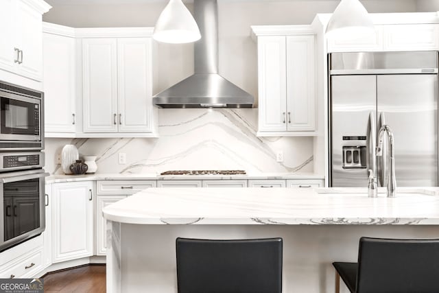 1065 Peachtree St NE Unit 3105, Atlanta, GA 30309 - kitchen featuring built in appliances, wall chimney range hood, a breakfast bar, white cabinets, and light stone countertops