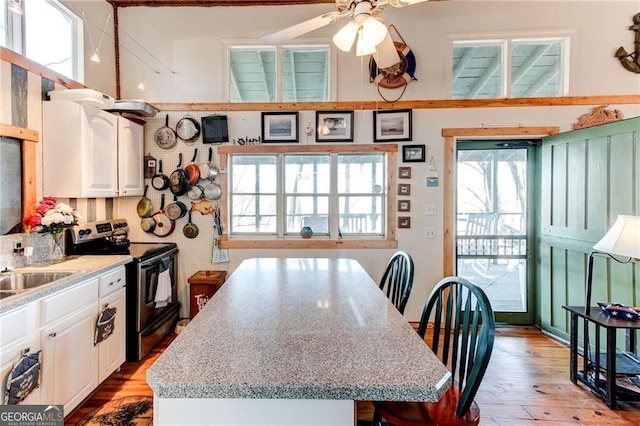 kitchen featuring light wood finished floors, stainless steel electric stove, white cabinets, and a center island