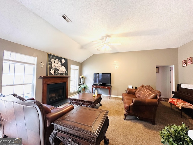 living area featuring visible vents, a ceiling fan, lofted ceiling, a fireplace with flush hearth, and carpet flooring