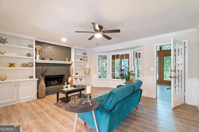 living room with a brick fireplace, wainscoting, and light wood finished floors