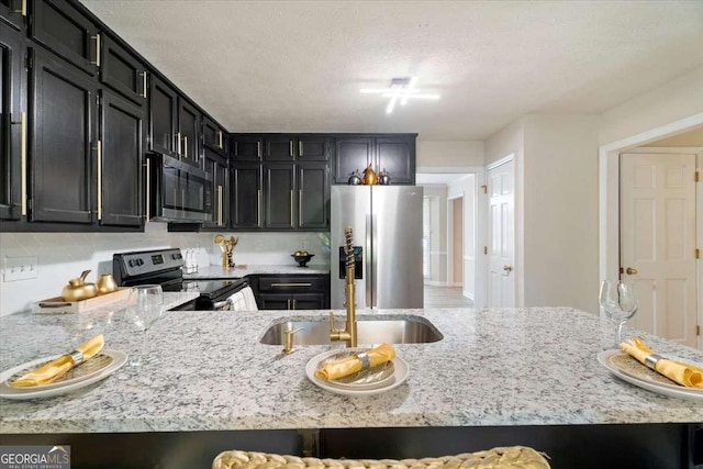 kitchen featuring light stone counters, dark cabinets, stainless steel appliances, a textured ceiling, and a sink