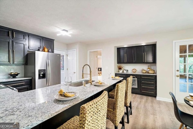 kitchen featuring a breakfast bar, light wood-style flooring, light stone countertops, dark cabinets, and stainless steel fridge with ice dispenser