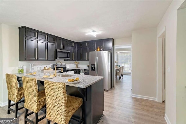 kitchen with a breakfast bar area, light wood finished floors, stainless steel appliances, a peninsula, and baseboards