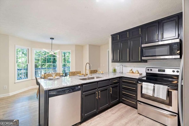 kitchen with light wood finished floors, appliances with stainless steel finishes, a sink, dark cabinets, and a peninsula