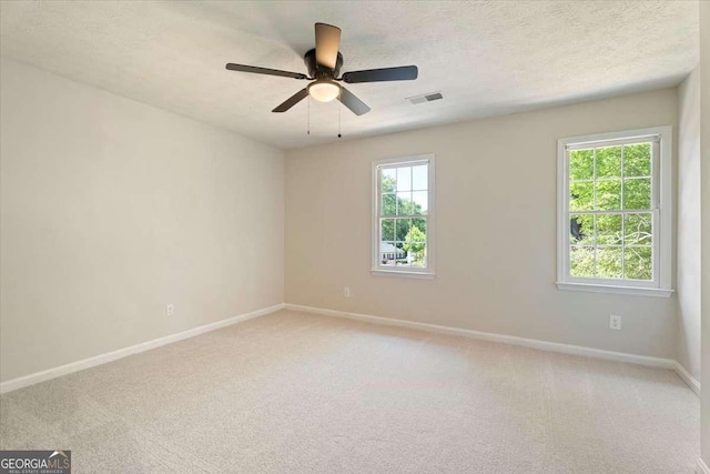 spare room featuring light colored carpet, visible vents, ceiling fan, a textured ceiling, and baseboards