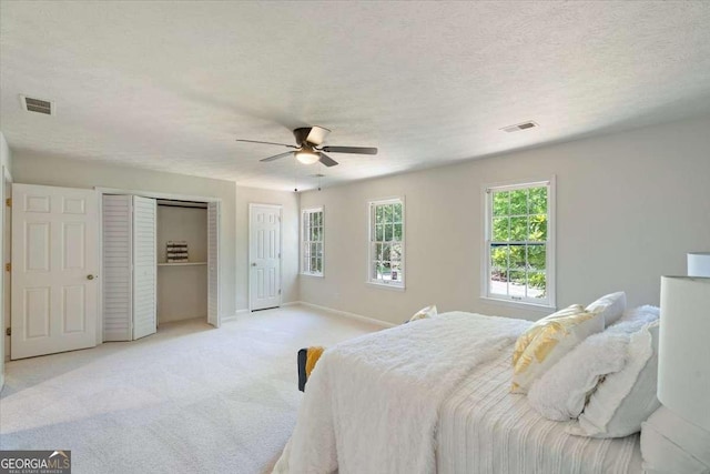 bedroom featuring a ceiling fan, light carpet, visible vents, and a textured ceiling