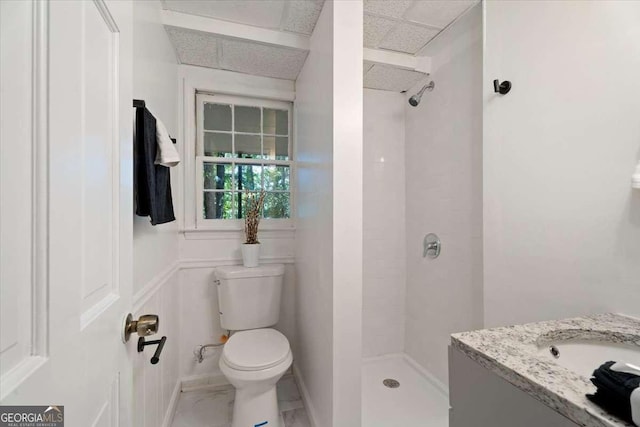 bathroom with tiled shower, a paneled ceiling, vanity, and toilet