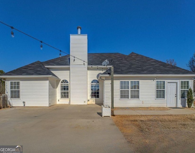 rear view of house with driveway, a chimney, and a patio area