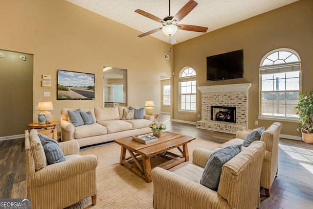 living room with baseboards, a ceiling fan, a tiled fireplace, wood finished floors, and high vaulted ceiling