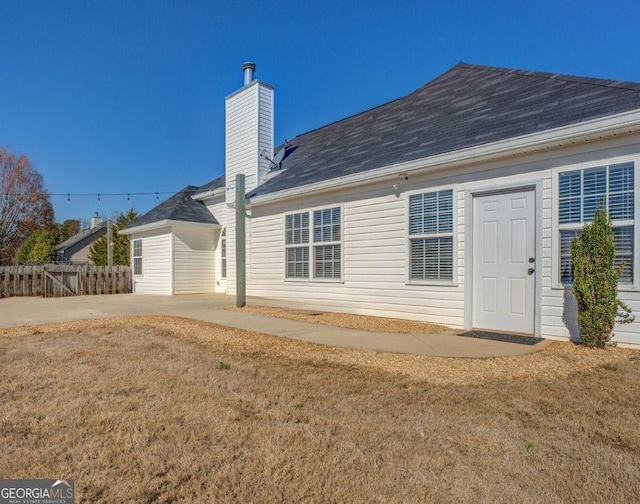 back of house with fence, a chimney, and a lawn