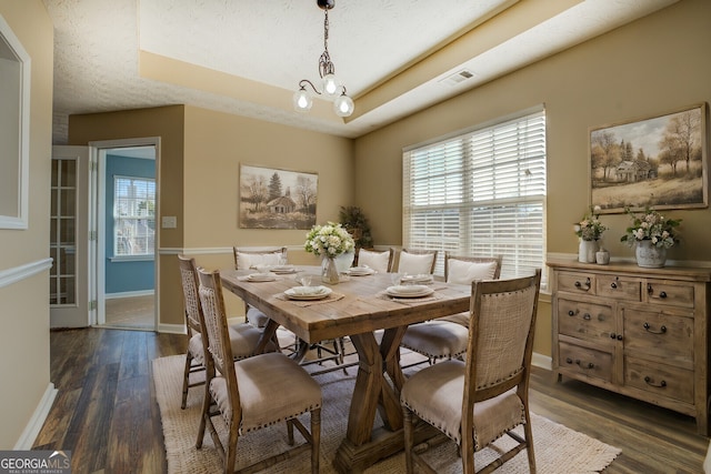 dining area featuring a raised ceiling, visible vents, baseboards, and wood finished floors