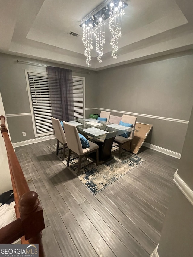 dining area with a tray ceiling, wood finished floors, visible vents, and baseboards