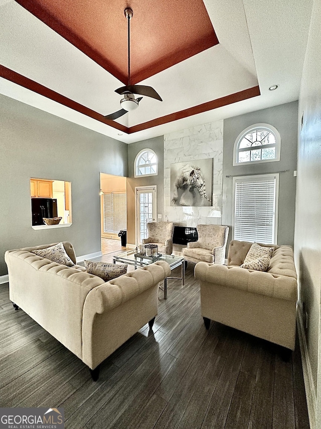 living area with a towering ceiling, ceiling fan, a raised ceiling, and dark wood-style flooring