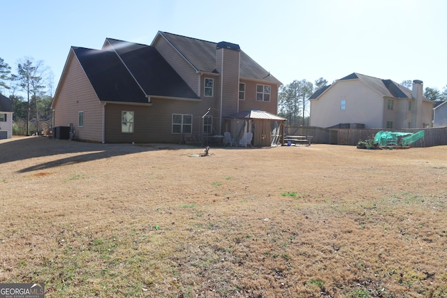 back of house with a chimney, a lawn, a gazebo, central AC unit, and fence