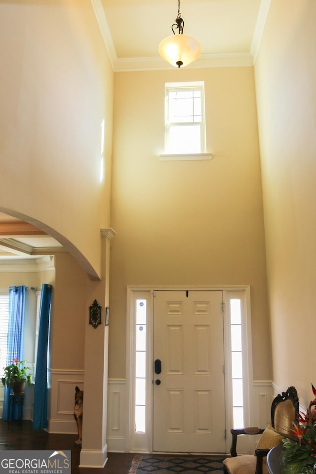 foyer entrance featuring a wainscoted wall, arched walkways, and ornamental molding