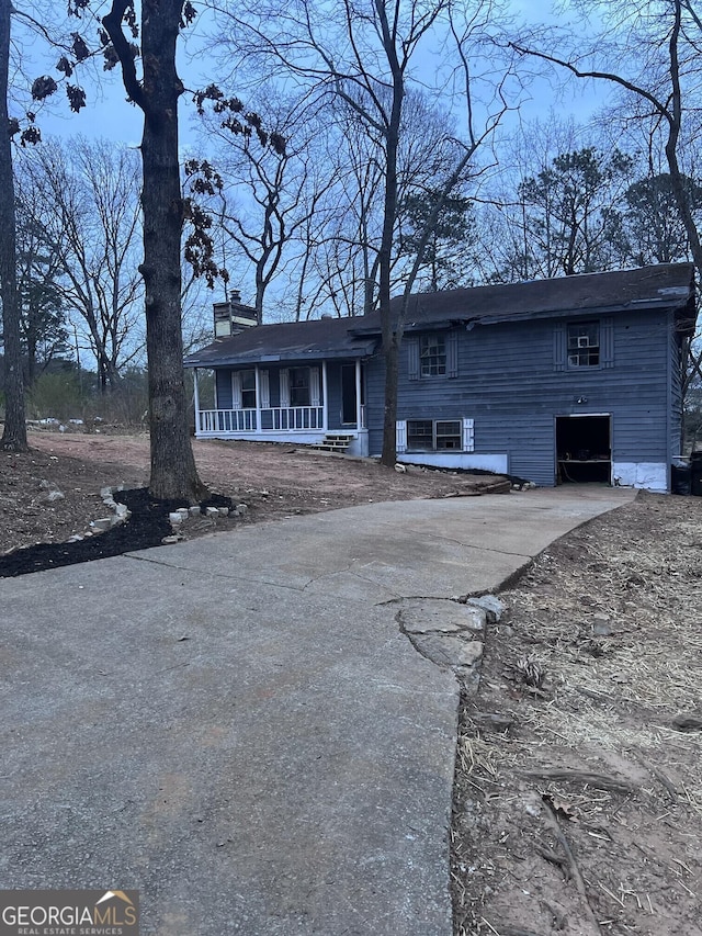 view of front of home with driveway, covered porch, a garage, and a chimney