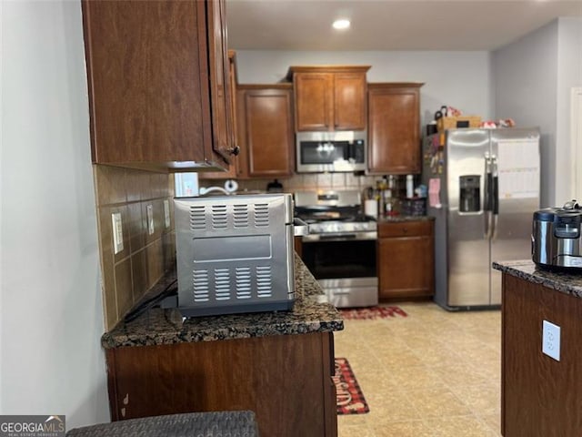 kitchen featuring recessed lighting, appliances with stainless steel finishes, backsplash, light floors, and dark stone countertops