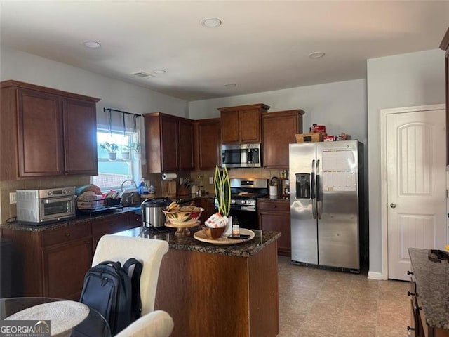 kitchen with a toaster, dark stone counters, decorative backsplash, a center island, and stainless steel appliances