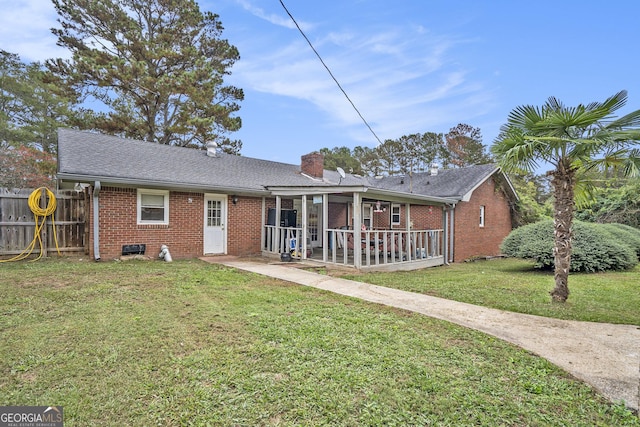 rear view of house with fence, a yard, roof with shingles, brick siding, and a chimney