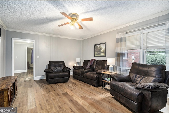 living area with wood-type flooring, ornamental molding, a ceiling fan, a textured ceiling, and baseboards