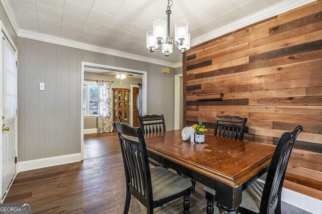 dining room featuring ceiling fan with notable chandelier, wood walls, wood finished floors, baseboards, and ornamental molding