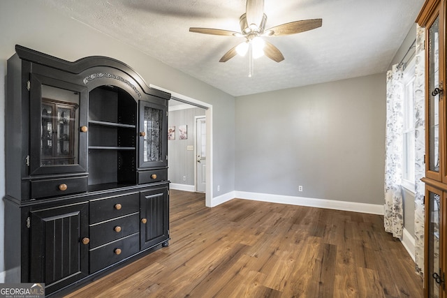 interior space featuring ceiling fan, dark wood-type flooring, a textured ceiling, and baseboards