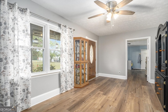 dining space with ceiling fan, a textured ceiling, baseboards, and wood finished floors