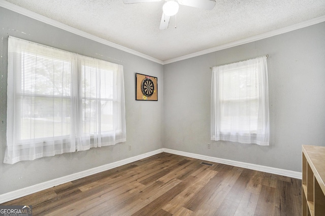 empty room featuring dark wood-style flooring, visible vents, ornamental molding, a textured ceiling, and baseboards