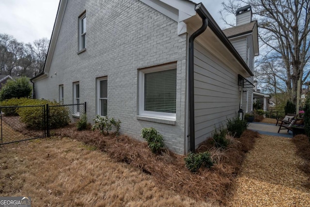 view of property exterior featuring a chimney, fence, a patio, and brick siding