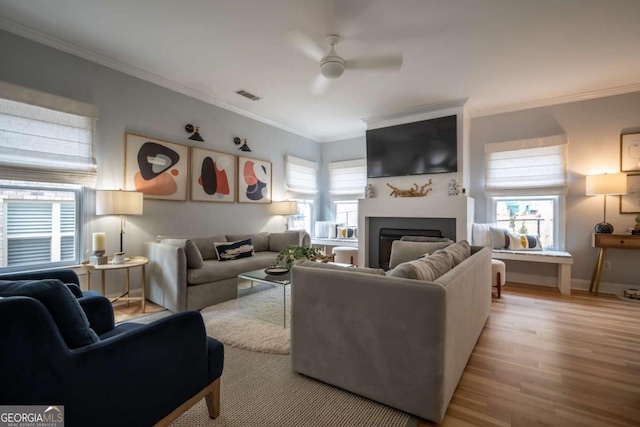 living room with plenty of natural light, visible vents, wood finished floors, crown molding, and a fireplace