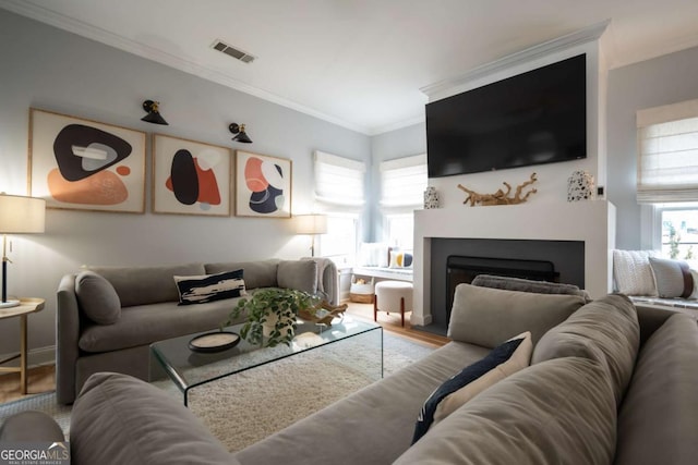 living area with a fireplace, visible vents, crown molding, and wood finished floors