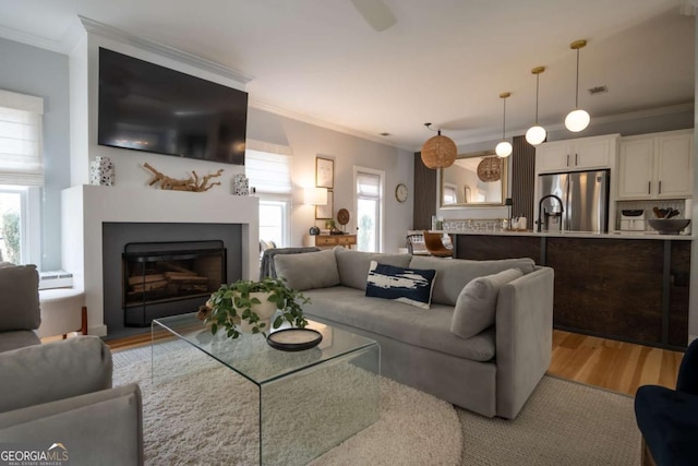 living area with light wood-type flooring, a fireplace, visible vents, and crown molding