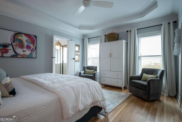 bedroom featuring light wood-style flooring, multiple windows, and a raised ceiling