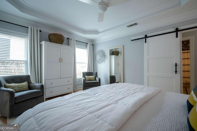 bedroom with ceiling fan, a barn door, visible vents, a tray ceiling, and crown molding