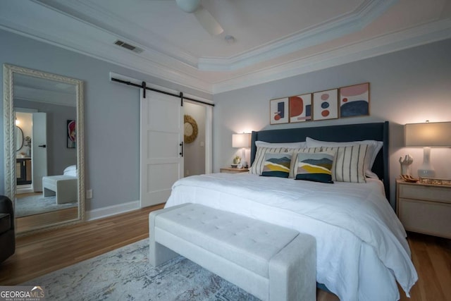 bedroom with a barn door, wood finished floors, visible vents, ornamental molding, and a tray ceiling