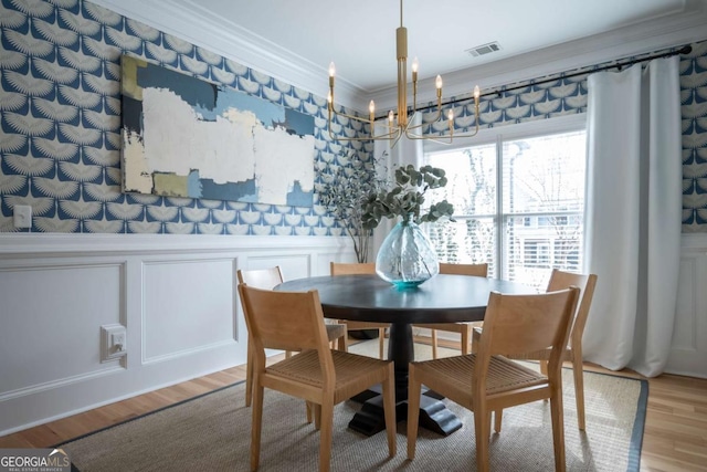 dining space with a notable chandelier, crown molding, a decorative wall, wainscoting, and wood finished floors