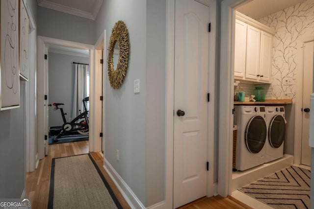 clothes washing area with wallpapered walls, light wood-style floors, cabinet space, and washing machine and clothes dryer