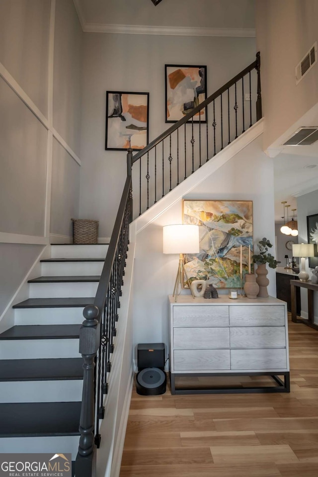 stairs with a towering ceiling, visible vents, crown molding, and wood finished floors