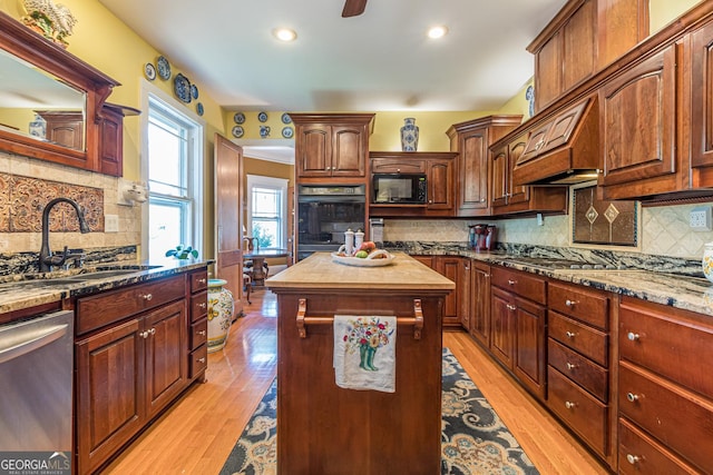 kitchen featuring light wood-style floors, dark stone counters, stainless steel appliances, and a sink