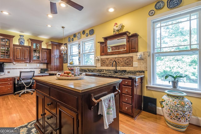 kitchen featuring butcher block counters, light wood-style floors, a center island, built in desk, and glass insert cabinets