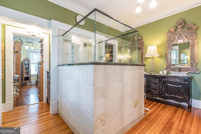 full bath featuring wood finished floors, ornamental molding, tiled shower, and vanity