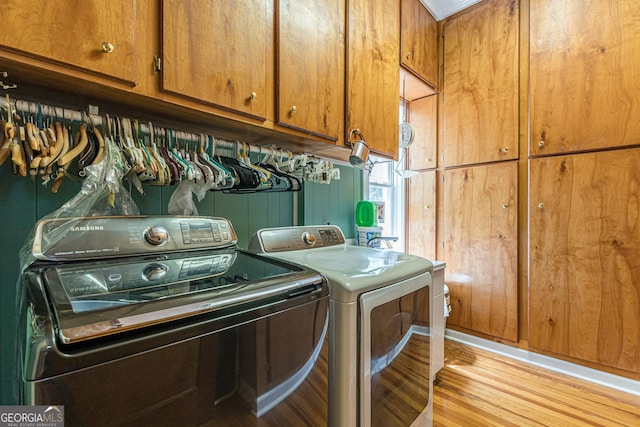 clothes washing area featuring light wood-style floors, cabinet space, and washer and clothes dryer