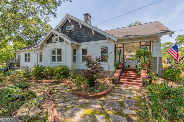 view of front facade featuring a wall mounted AC, a shingled roof, a chimney, and brick siding