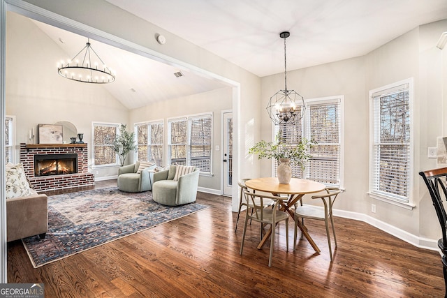 dining room featuring a brick fireplace, an inviting chandelier, and wood finished floors