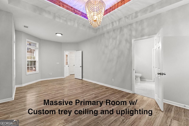 unfurnished room with a tray ceiling, wood finished floors, and baseboards