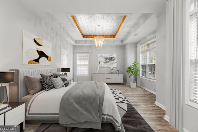 bedroom featuring a tray ceiling, multiple windows, baseboards, and wood finished floors