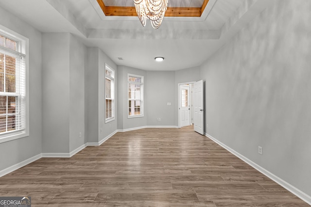 foyer entrance with an inviting chandelier, baseboards, a tray ceiling, and wood finished floors