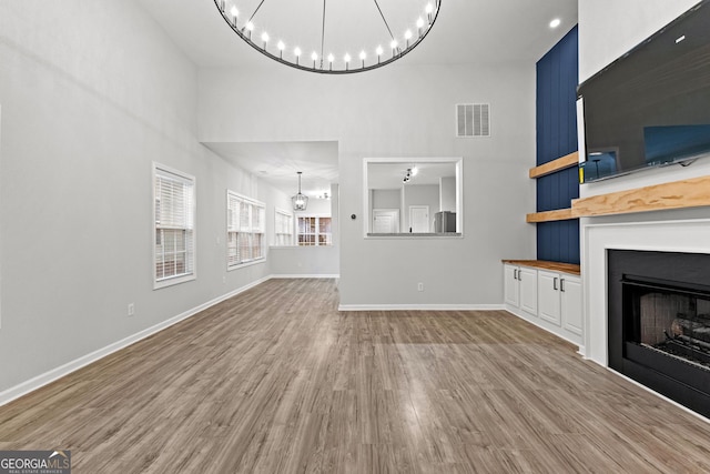 unfurnished living room with a notable chandelier, a fireplace, wood finished floors, visible vents, and baseboards