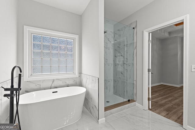 bathroom featuring marble finish floor, a wainscoted wall, tile walls, a marble finish shower, and a freestanding bath