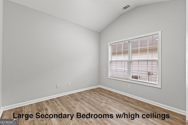 empty room with visible vents, vaulted ceiling, baseboards, and wood finished floors